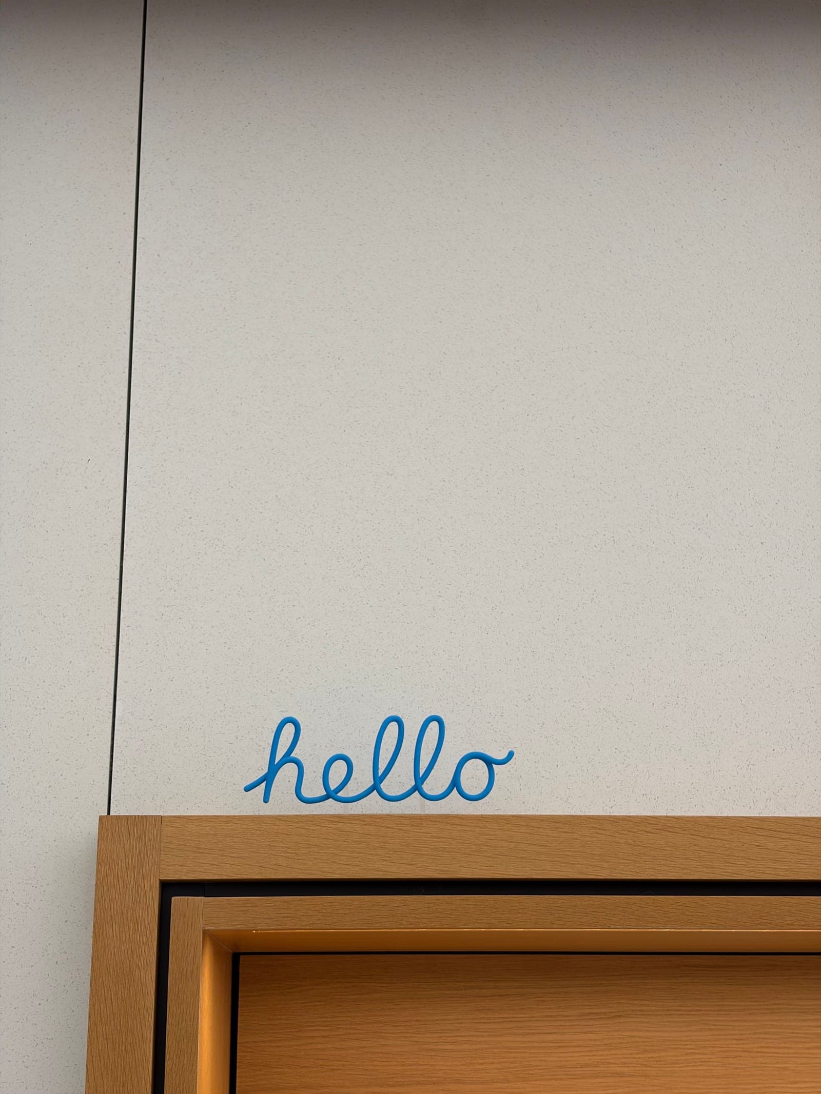 The word hello in blue script above a wooden door frame at an Apple Store.
